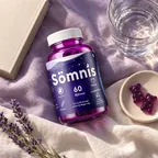 Burk med Sömnis gummibjörnar på sängen bredvid ett glas vatten och lavendel